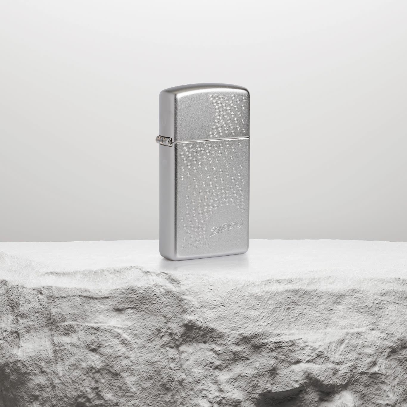 Lifestyle image of Slim® Zippo Dot Design Satin Chrome Windproof Lighter standing on a white rock pedestal.