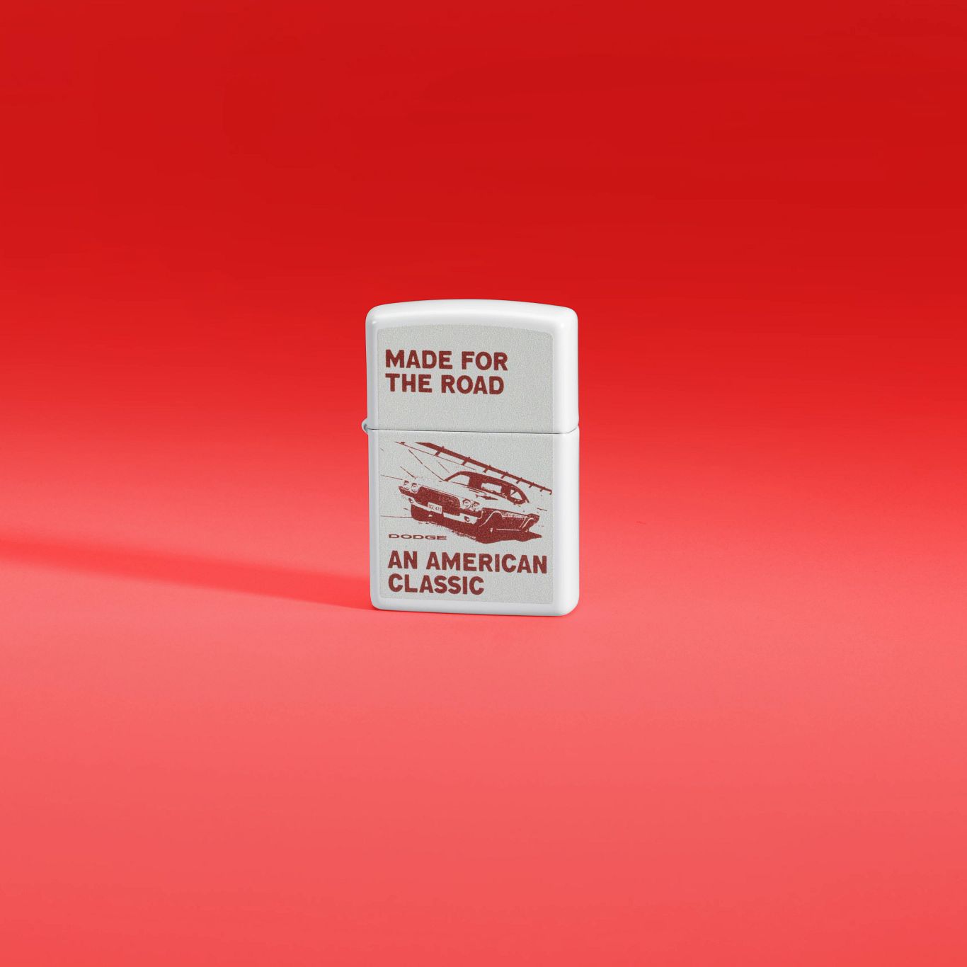 Lifestyle image of Zippo Dodge Made for the Road Design White Matte Windproof Lighter standing against a red background.