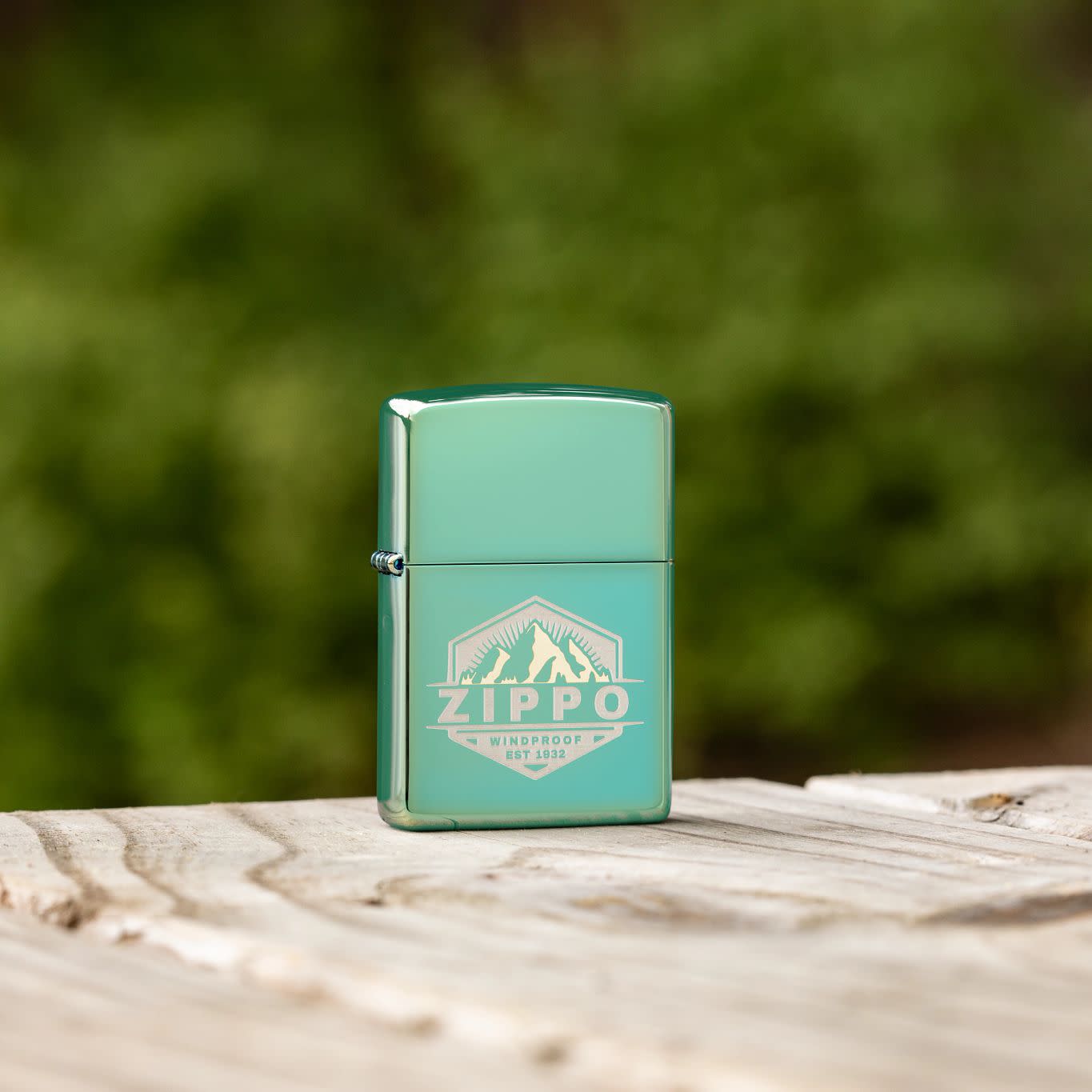 Lifestyle image of Zippo Badge Design High Polish Green Windproof Lighter standing on a wooden deck with greenery blurred in the background.