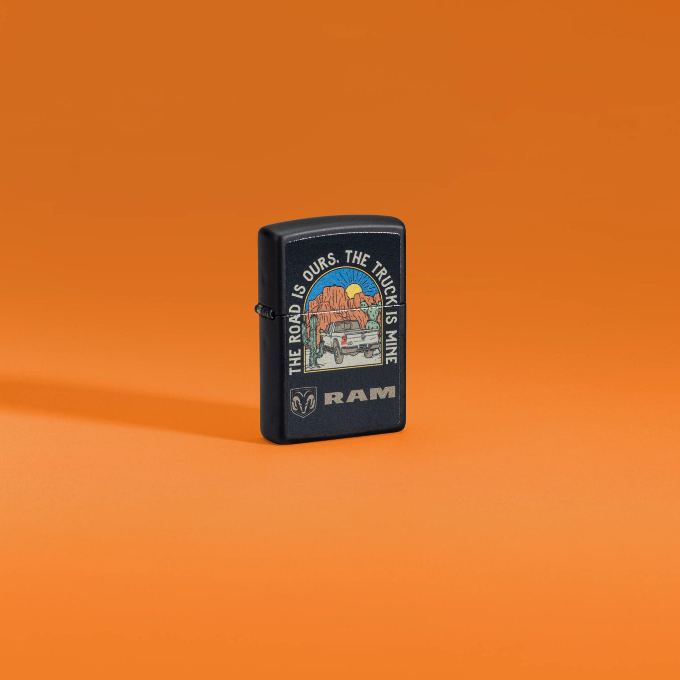 Lifestyle image of Zippo Ram The Truck is Mine Design Black Matte Windproof Lighter standing against an orange background.