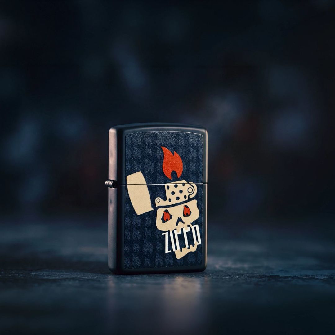 Lifestyle image of Zippo Skull and Flames Design Black Matte Windproof Lighter standing on a smooth black surface showing the front and hinge side of the lighter with a black background.