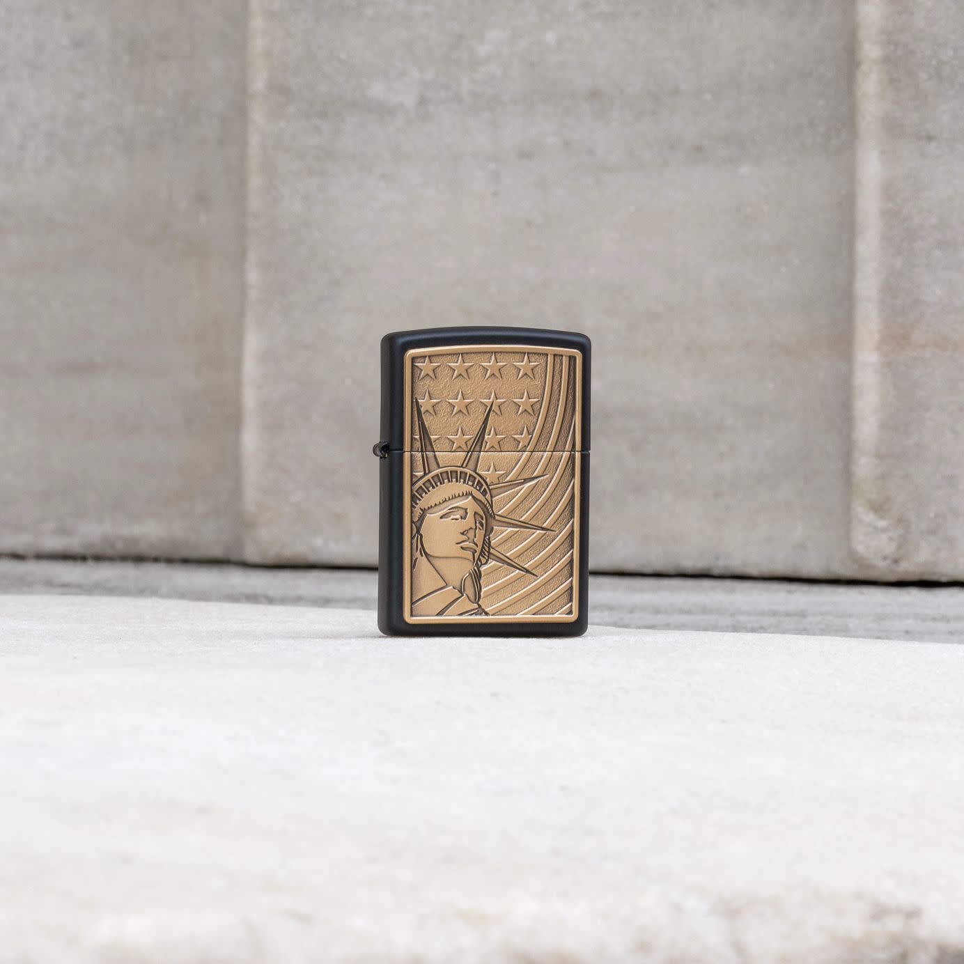 Lifestyle image of Zippo Lady Liberty Emblem Black Matte Windproof Lighter standing in front of a cement wall.