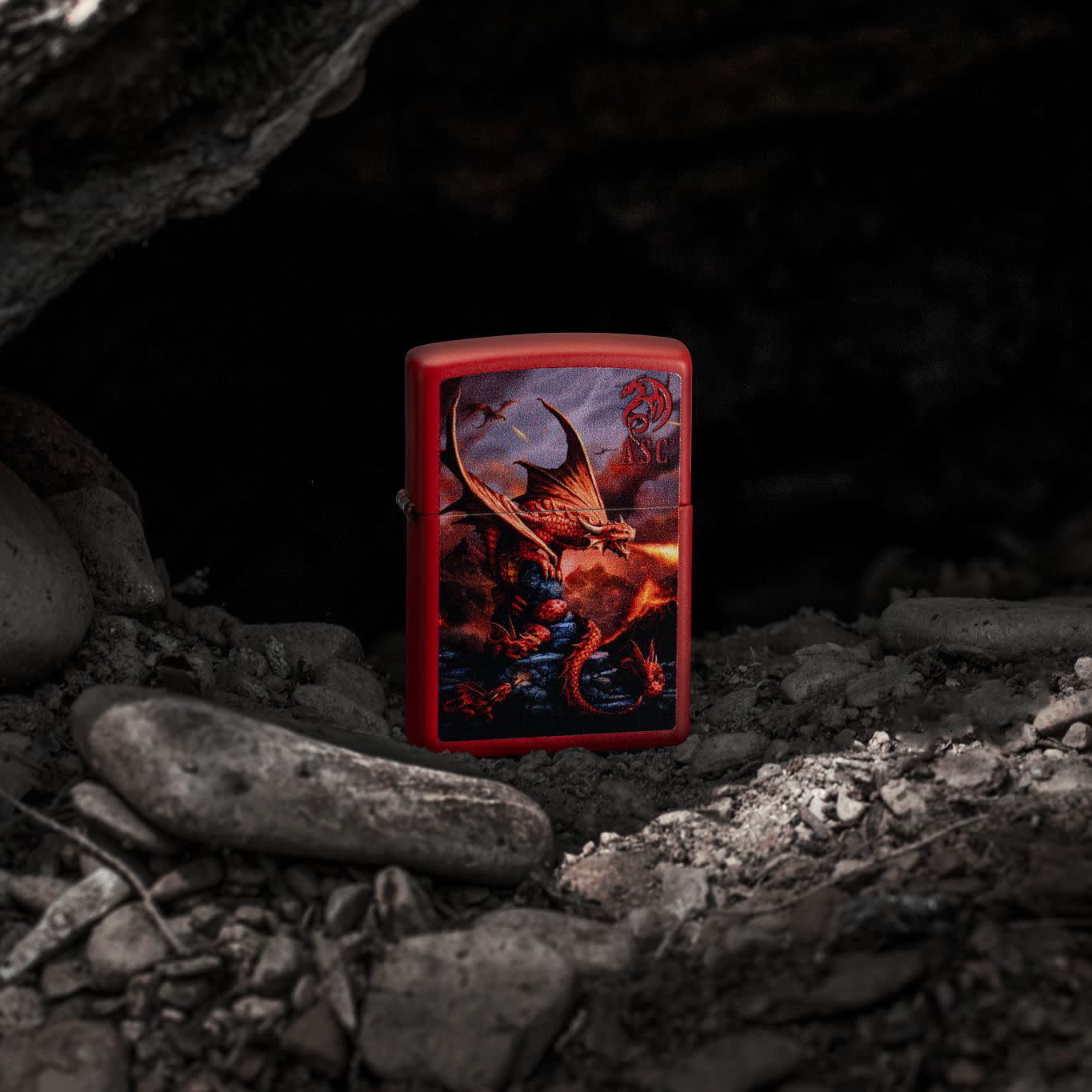 Lifestyle image of Zippo Anne Stokes Fire Dragon Design Red Matte Windproof Lighter standing on rocks set in an alcove.