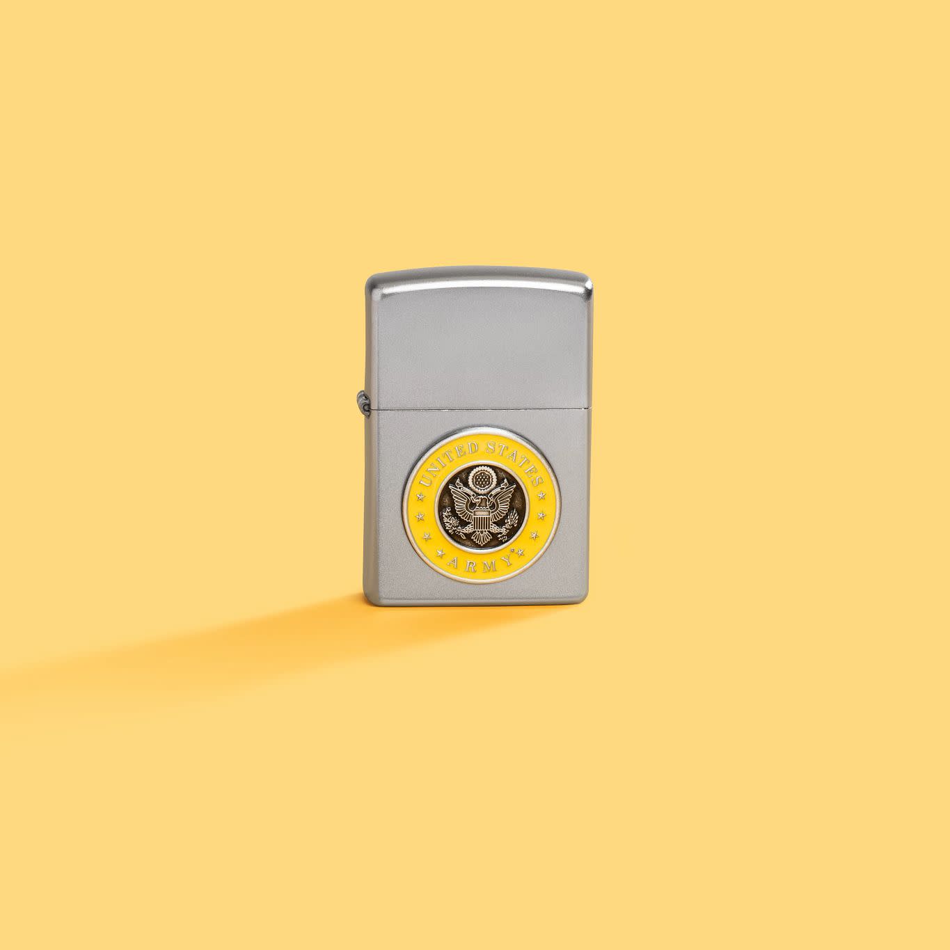 Lifestyle image of Zippo United States Army® Emblem Satin Chrome Windproof Lighter on a light yellow background.
