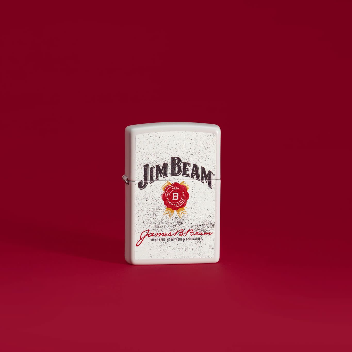 Lifestyle image of Zippo Jim Beam® Rosette Design White Matte Windproof Lighter standing with a deep red background.
