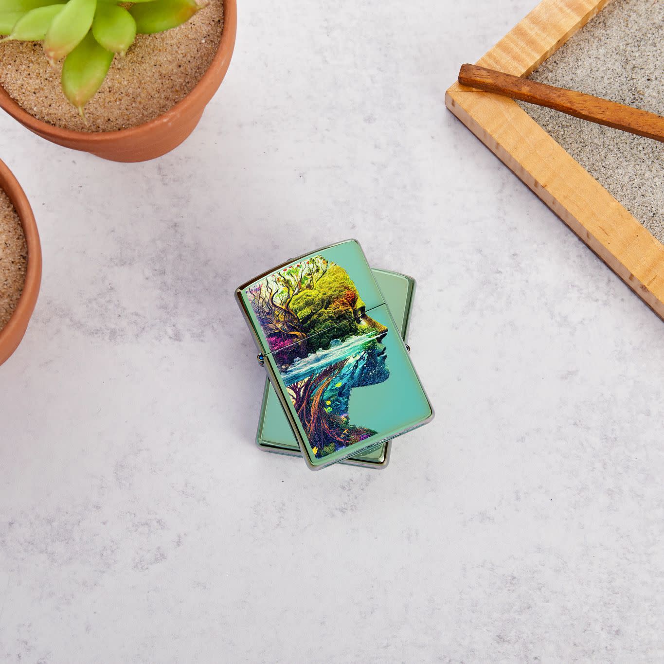 Lifestyle image of two Zippo One with Nature Design High Polish Green Windproof Lighters stacked one on top of the other with succulents in the background.
