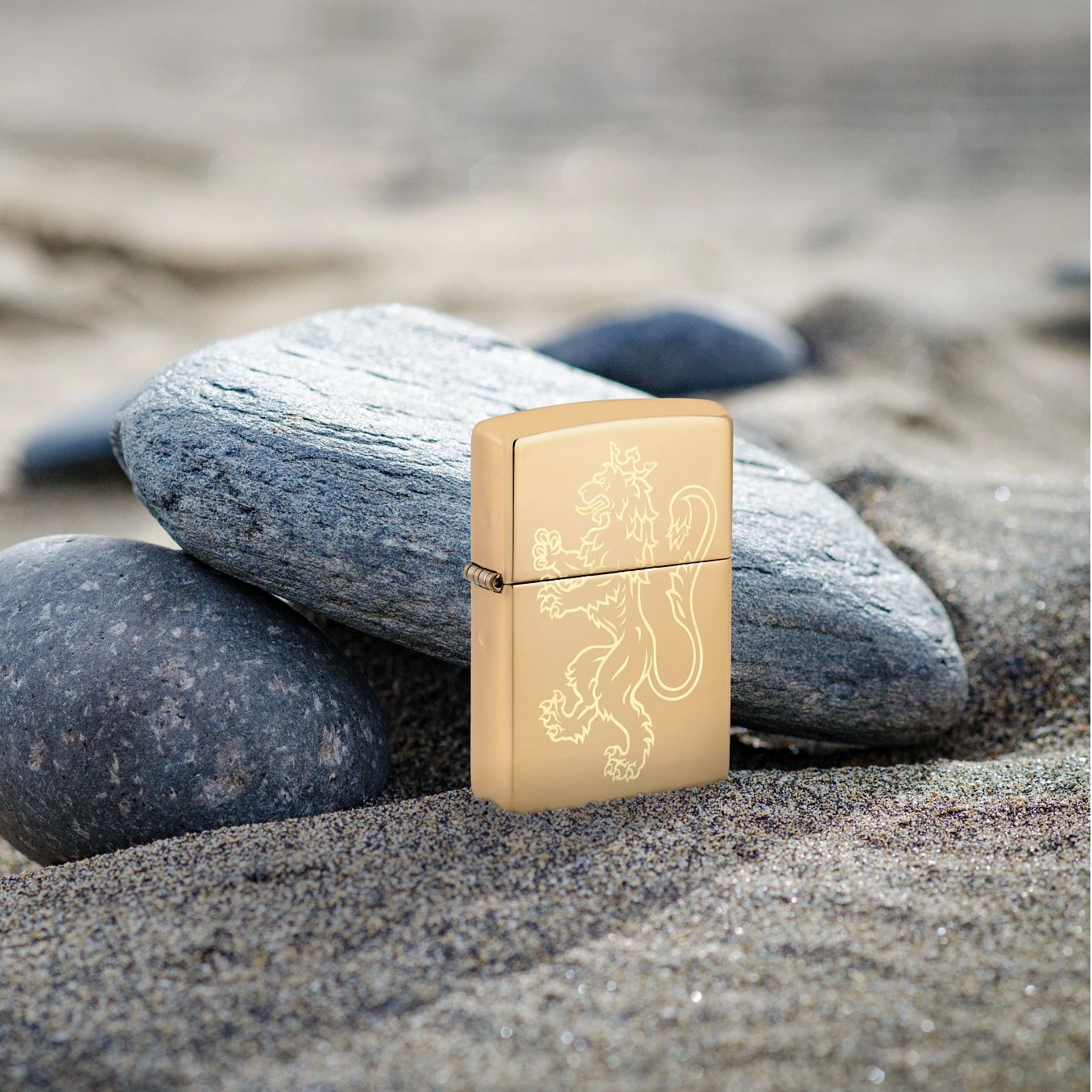 Lifestyle image of Zippo Fighting Lion Design High Polish Brass Windproof Lighter standing in the sand while leaning against a river rock.