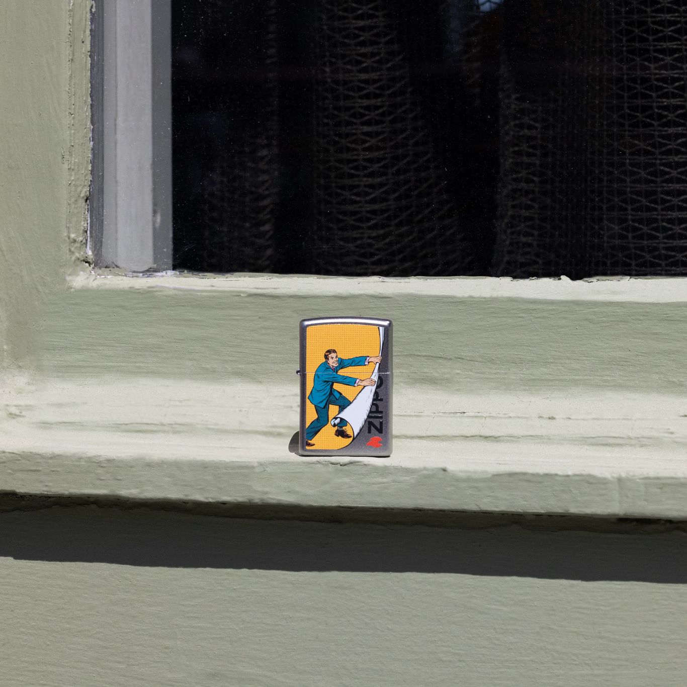 Lifestyle image of Zippo Reveal Design Satin Chrome Windproof Lighter standing on a painted window ledge.
