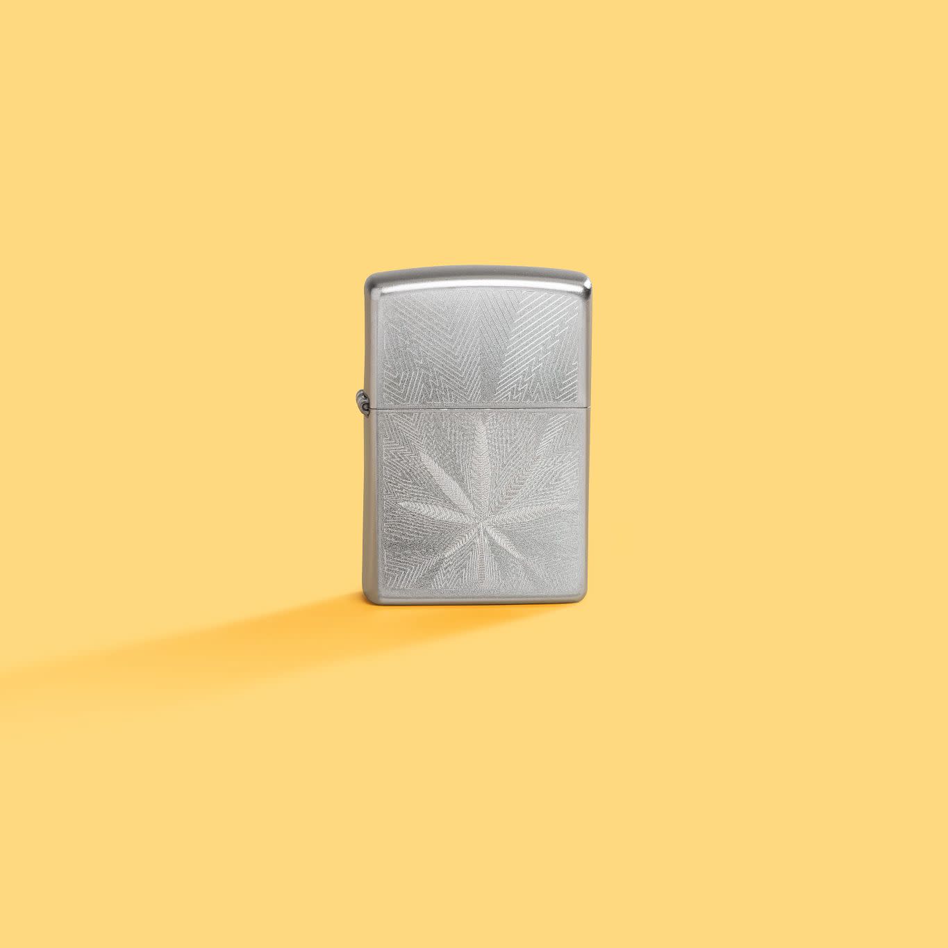 Lifestyle image of Zippo Luxury Leaf Design Satin Chrome Windproof Lighter standing in a yellow scene.
