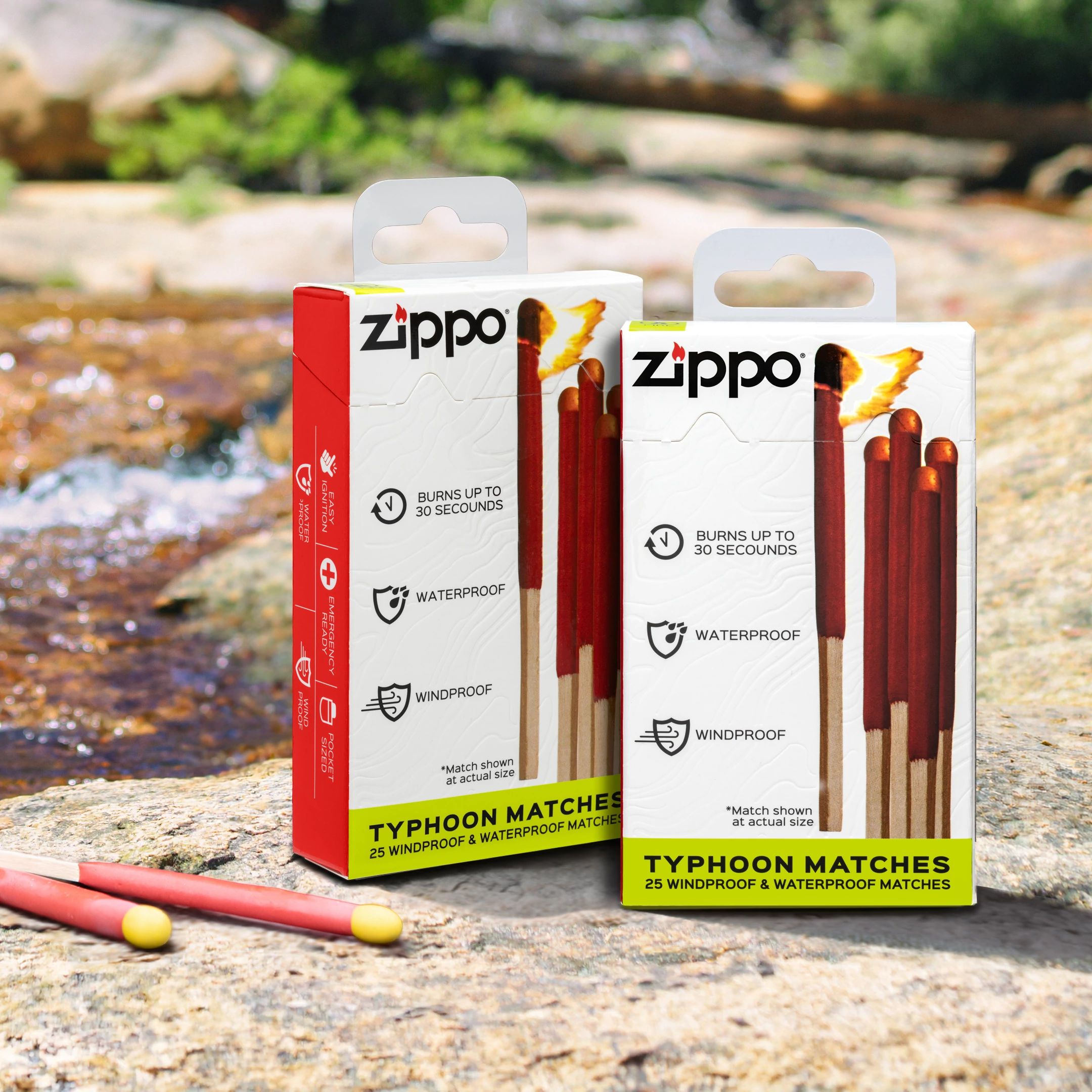 Two packages of Zippo Typhoon Matches and two loose matches displayed on a rock beside a flowing stream in an outdoor natural setting.