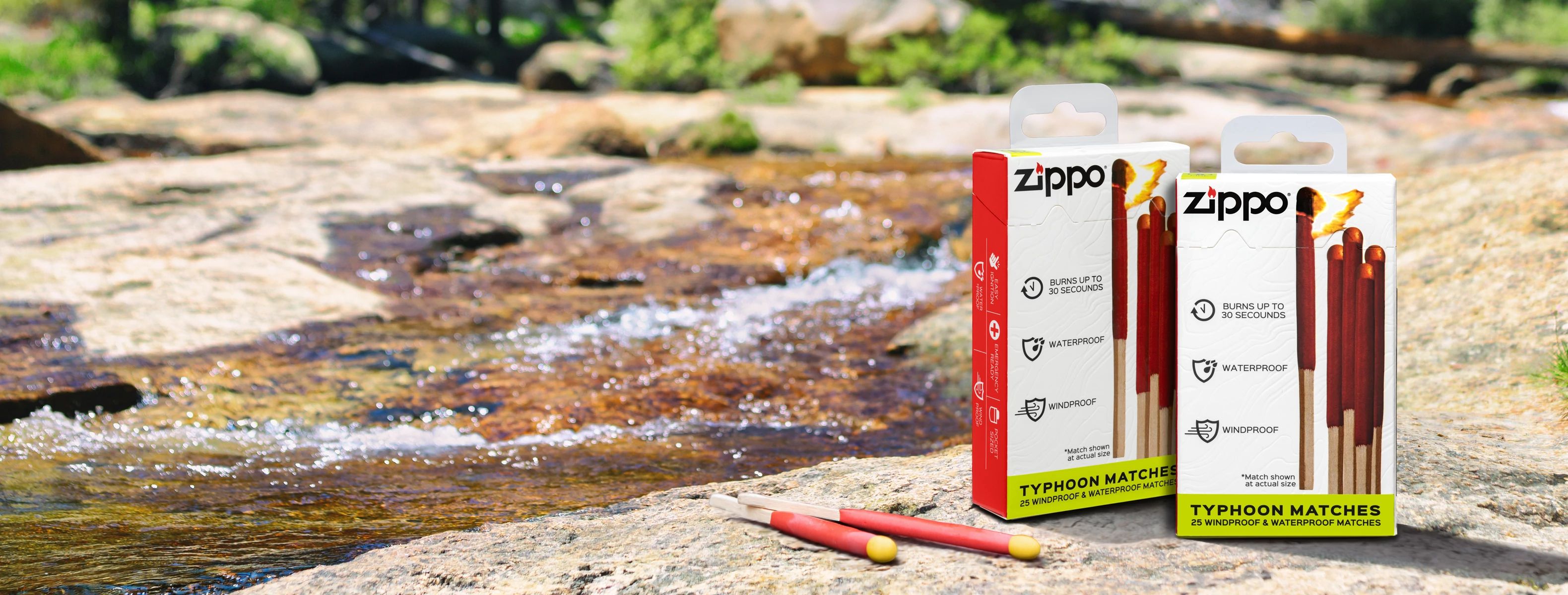 Two packages of Zippo Typhoon Matches and two loose matches displayed on a rock beside a flowing stream in an outdoor natural setting.