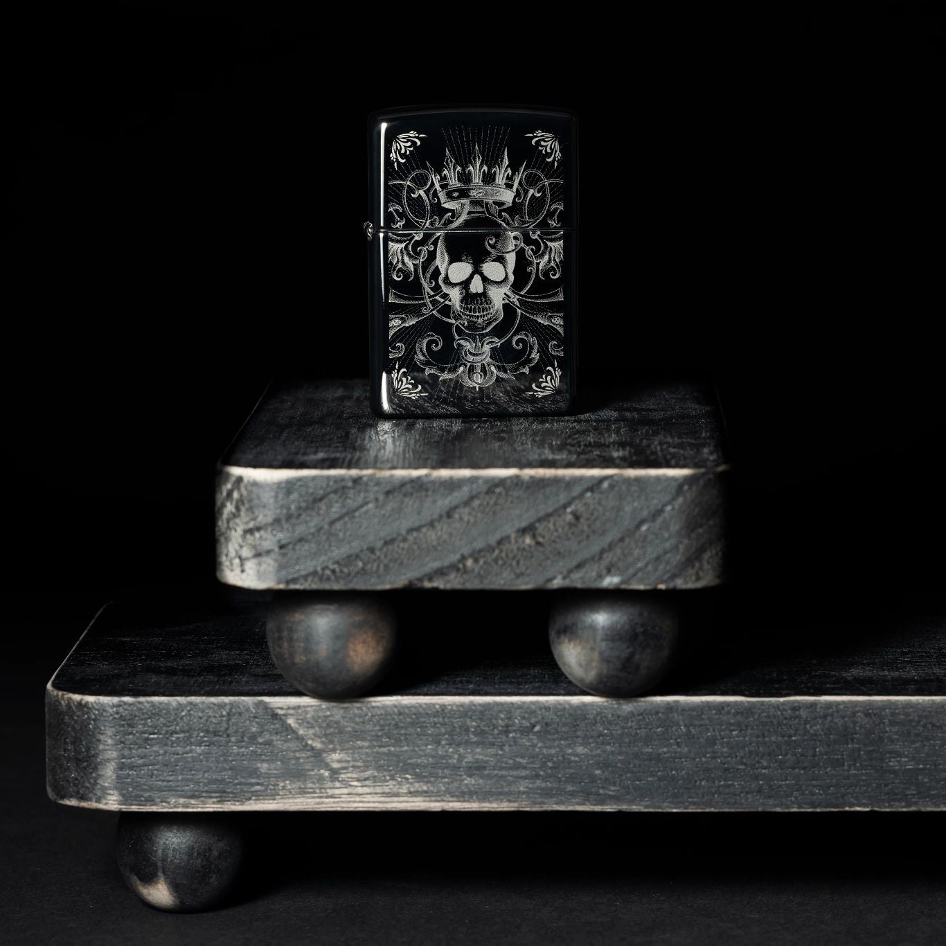 Lifestyle image of Zippo Royal Skull Design High Polish Black Windproof Lighter standing on dark platforms.