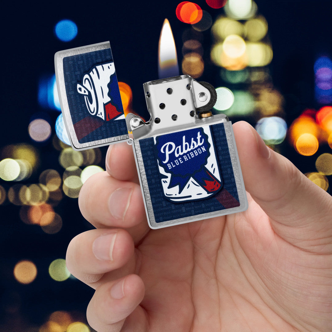 Zippo Pabst Blue Ribbon® Can Art Design Brushed Chrome Windproof Lighter lit in hand.