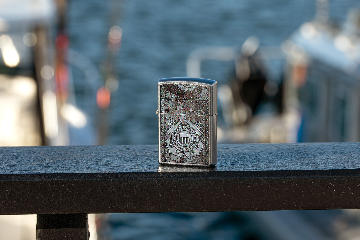 Lifestyle image of U.S. Coast Guard Windproof Lighter sitting on black post with water landscape