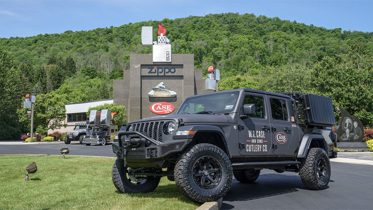 The Case Jeep is parked outdoors in front of the museum, with a forested hill in the background. The vehicle has off-road tires, a front bull bar, and side text reading 'W.R. Case and Sons Cutlery Co.'