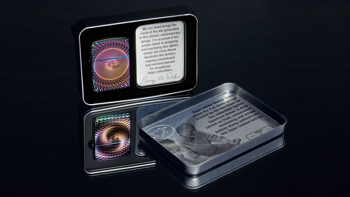 A decorative metal tin set displayed on a dark reflective surface, with one tin open to show a colorful circular lighter design and printed text, and another tin beside it showing a grayscale illustration and text.