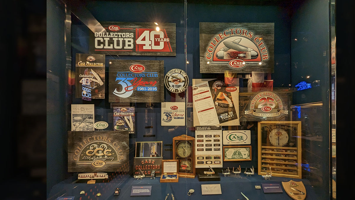 A glass display case showcasing a collection of vintage and modern signs, plaques, trophies, and memorabilia against a dark blue background.