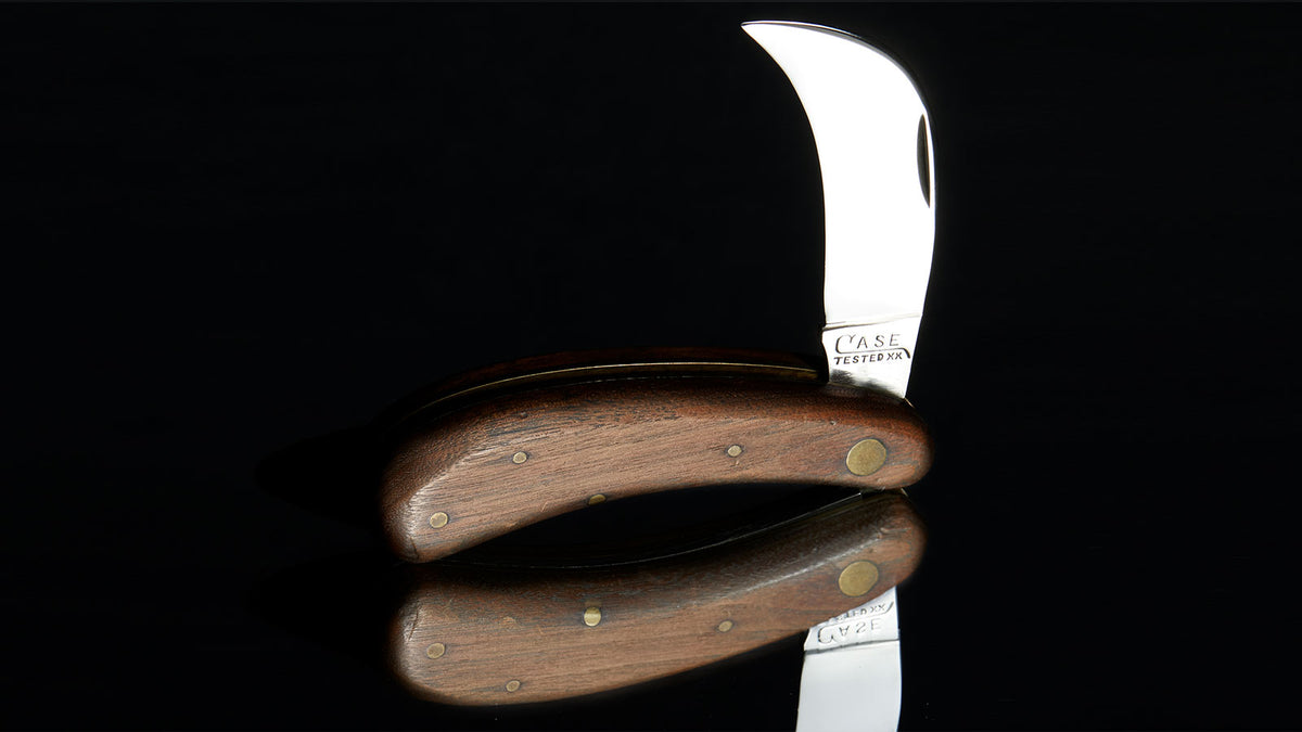 A folding pocket knife with a curved silver blade and a brown wooden handle, shown partially open against a solid black background with a reflection below.