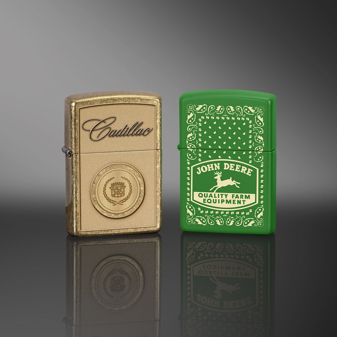 Two zippo lighters, one gold and one green, on a reflective surface with a gray background.