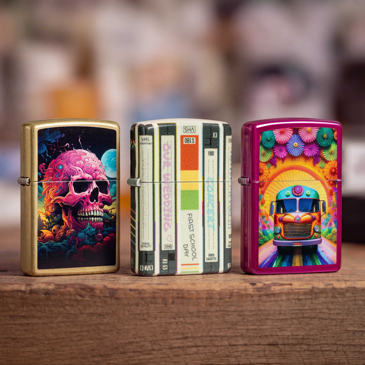 Three Zippo lighters. One with a skull on the front, the middle one is old-school styled, and the third one is pink with flowers and a bus on the front.