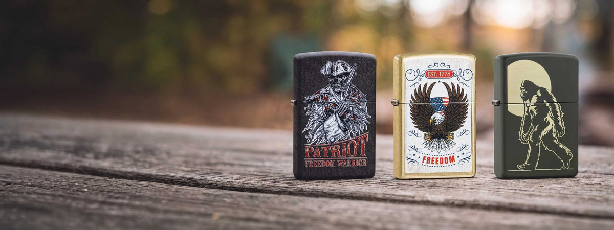 Three Zippo lighters on a wooden surface. First one says "Patriot Freedom Warrier', the middle one is an eagle on a white background, and the third is a Sasquatch.