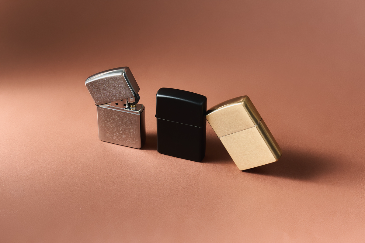 A silver, black and brass lighter in front of a tan background. The silver Zippo lighter has the lid opened.