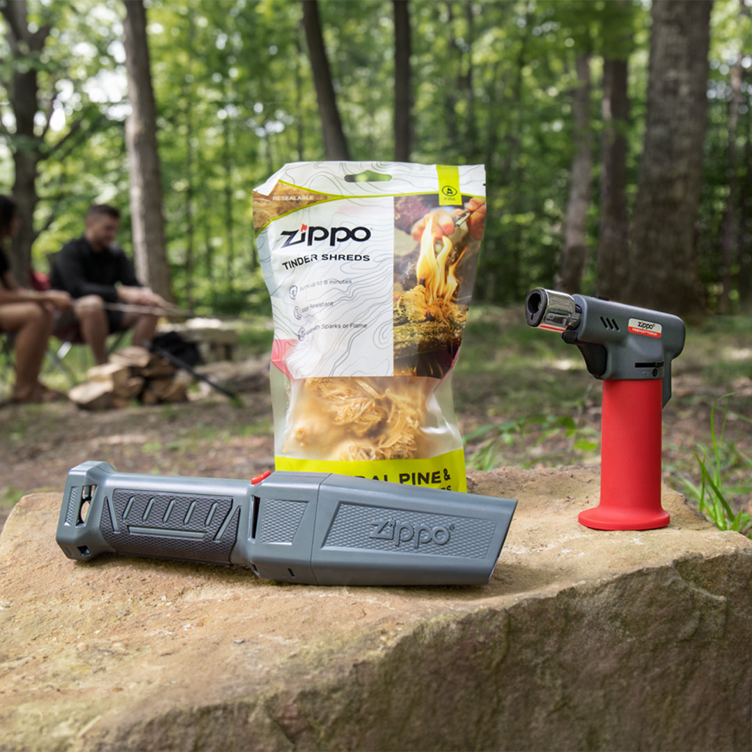 A Zippo FireFast® Bellows, FireFast®  Torch and Tinder Shreds on a rock with a campsite in the background.