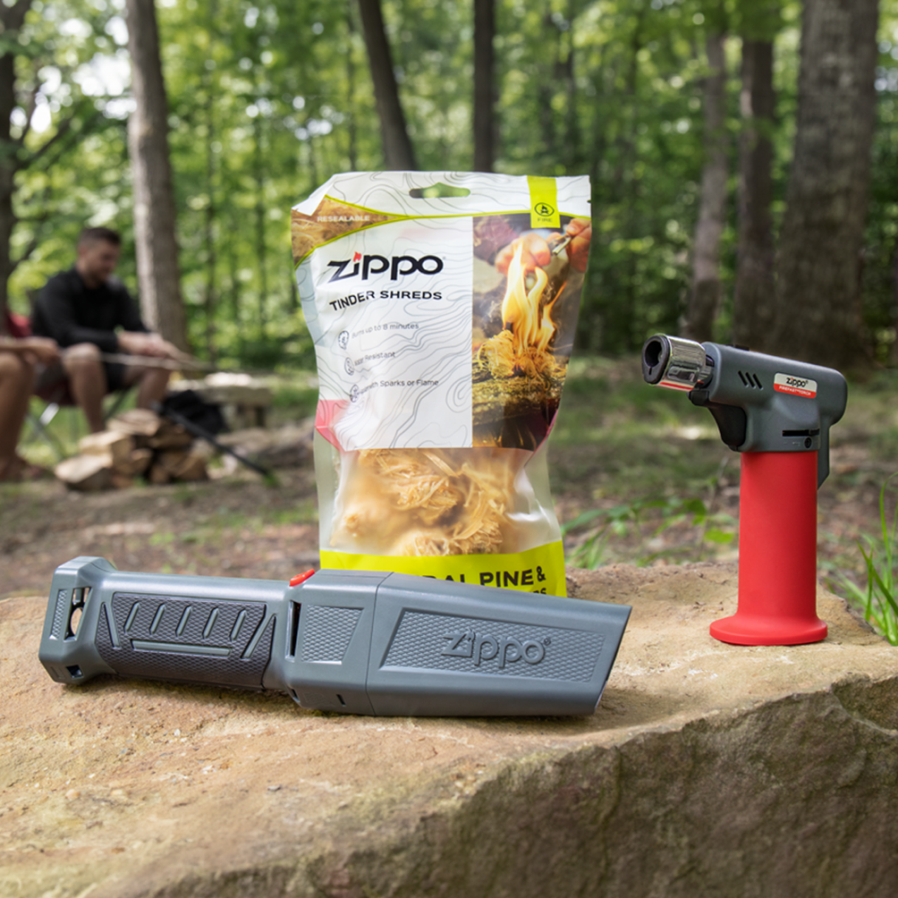 A Zippo FireFast® Bellows, FireFast®  Torch and Tinder Shreds on a rock with a campsite in the background.
