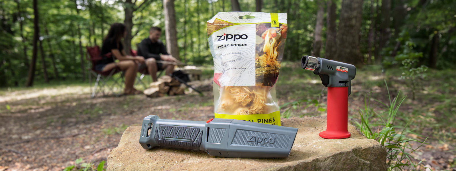 A Zippo FireFast® Bellows, Tinder Shreds and a FireFast®  Torch on a rock with a campsite in the background.

