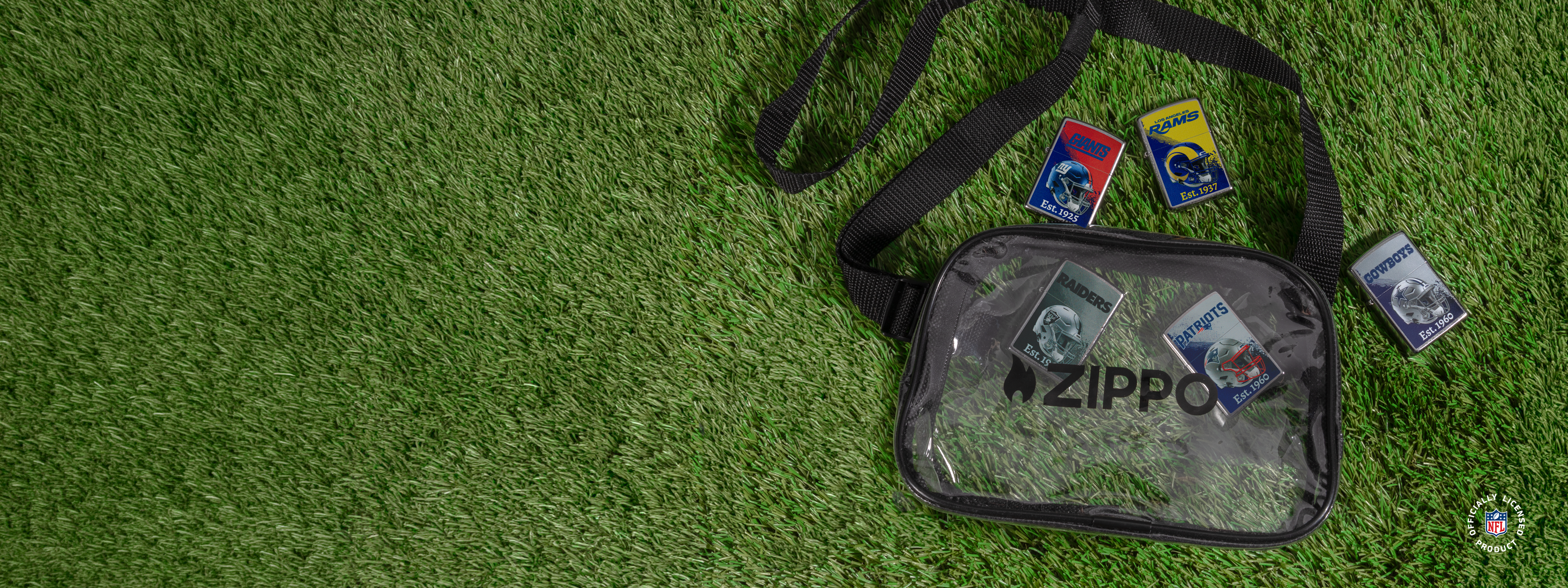 A clear Zippo bag with a black strap, laid flat on grass. The bag has ZIPPO printed on the front and contains five Zippo lighters around the bag.