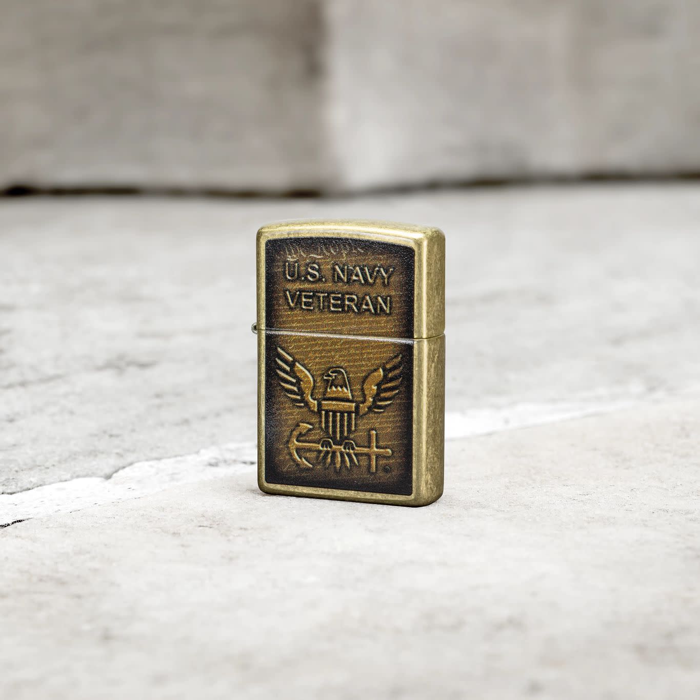 Lifestyle image of Zippo United States Navy® Street Brass Windproof Lighter standing on a grey tile floor.