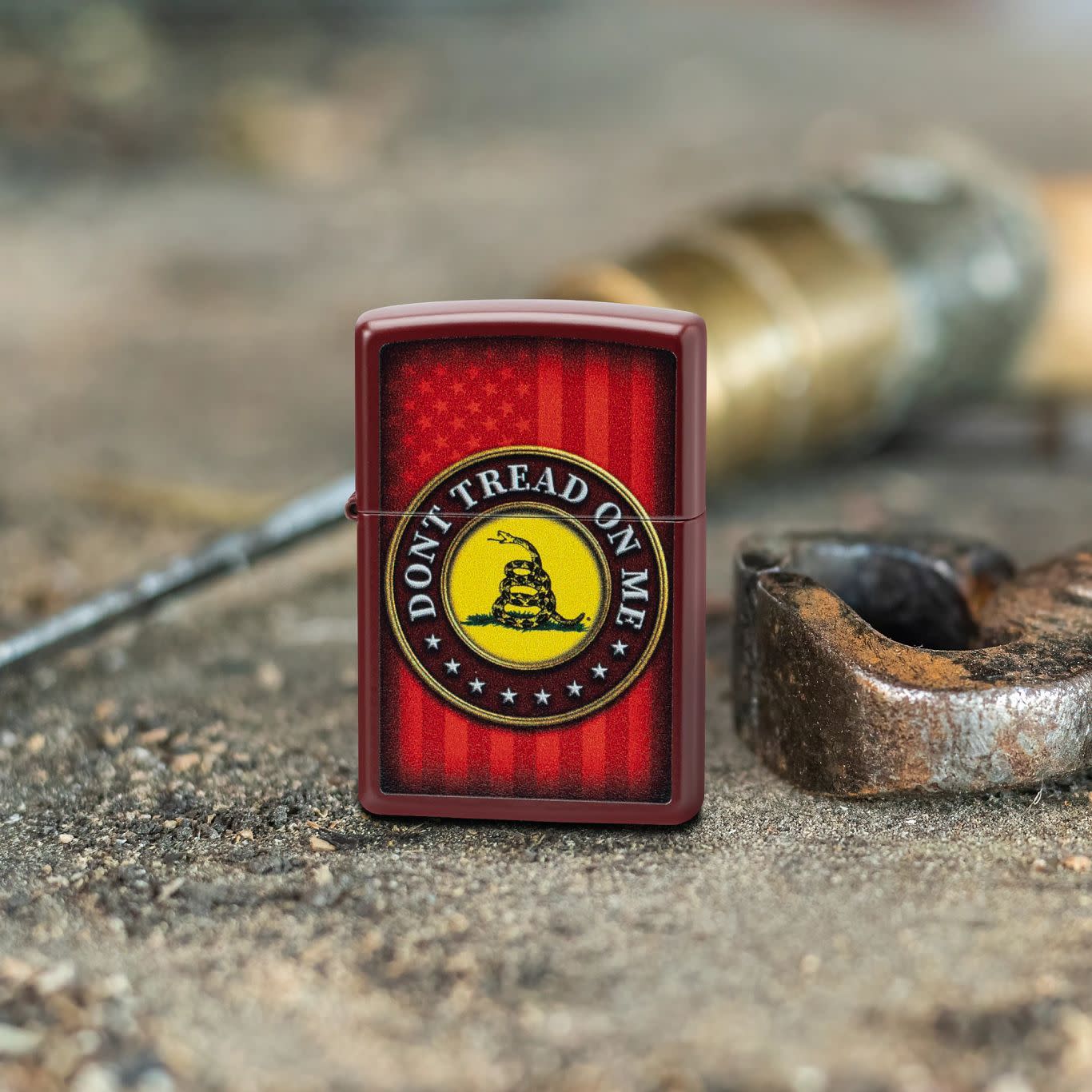 Lifestyle image of Zippo Dont Tread on Me® Merlot Windproof Lighter standing on a dirty surface with pliers and a screwdriver behind.