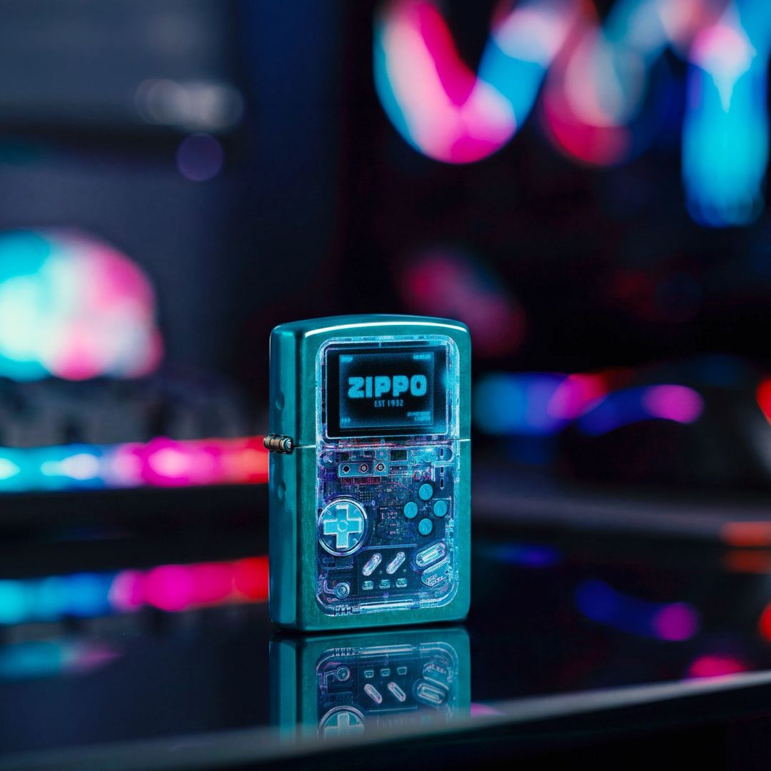 Lifestyle image of Zippo Game On Design Candy Teal Windproof Lighter standing on a dark surface showing the front and hinge side of the lighter with a neon gaming vibe background. 

