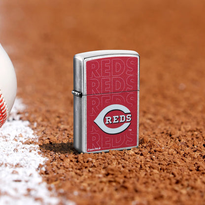 Lifestyle image of Zippo MLB® Cincinnati Reds Street Chrome Windproof Lighter standing in the dirt on a baseball field.