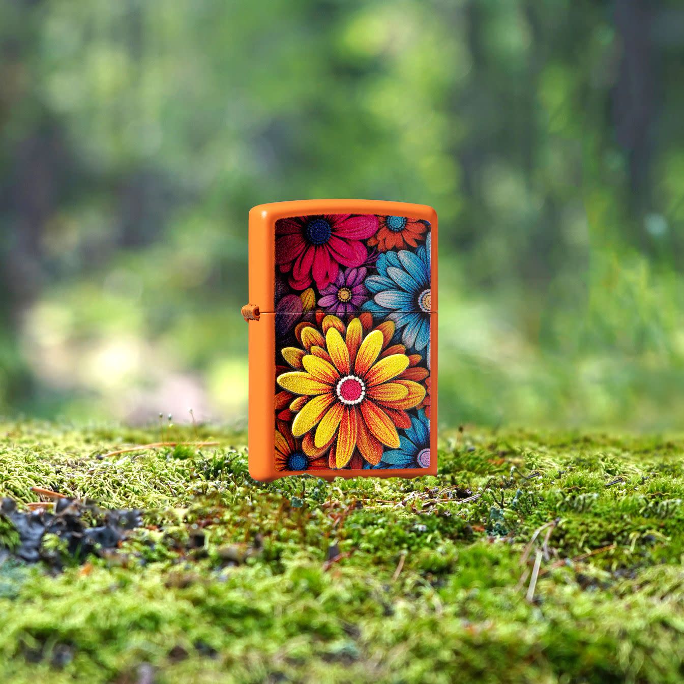 Lifestyle image of Zippo Flowers Design Orange Matte Windproof Lighter standing on a mossy ground with blurred greenery behind it.