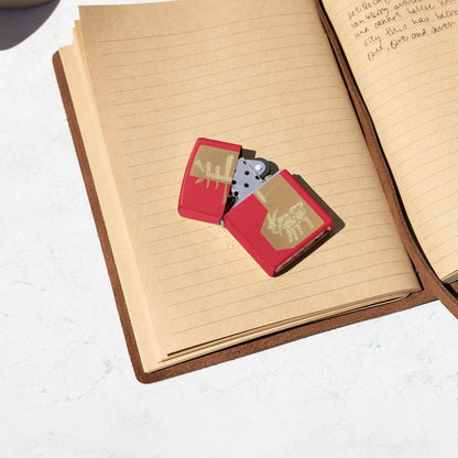 Lifestyle image of Zippo 2027 Year of the Sheep Design Red Matte Windproof Lighter lying slightly open on an open book showing the front and hinge side of the lighter. 

