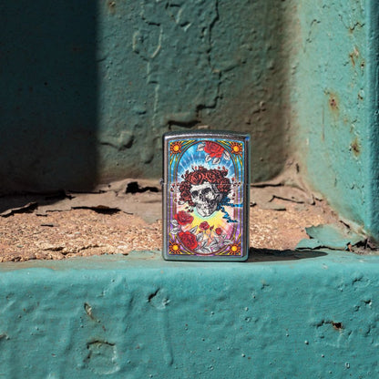 Lifestyle image of Zippo Grateful Dead Bertha Design Street Chrome Windproof Lighter standing on the edge of a teal concrete wall showing the front of the lighter.

