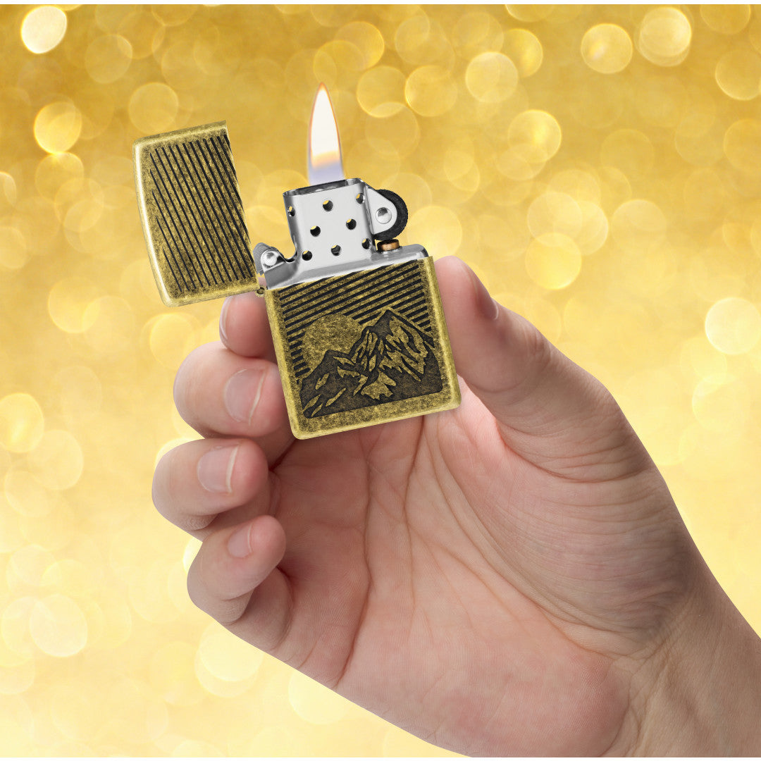 Zippo Etched Mountains Design Antique Brass Windproof Lighter lit in hand.