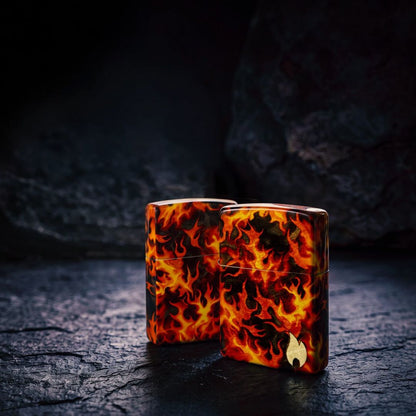 Lifestyle image of two Zippo Inferno Design 540 Matte Windproof Lighters standing on a black stone surface. One showing the back and non-hinge side of the lighter while the other is showing the front and non-hinge side of the lighter with two dark stones in the background. 

