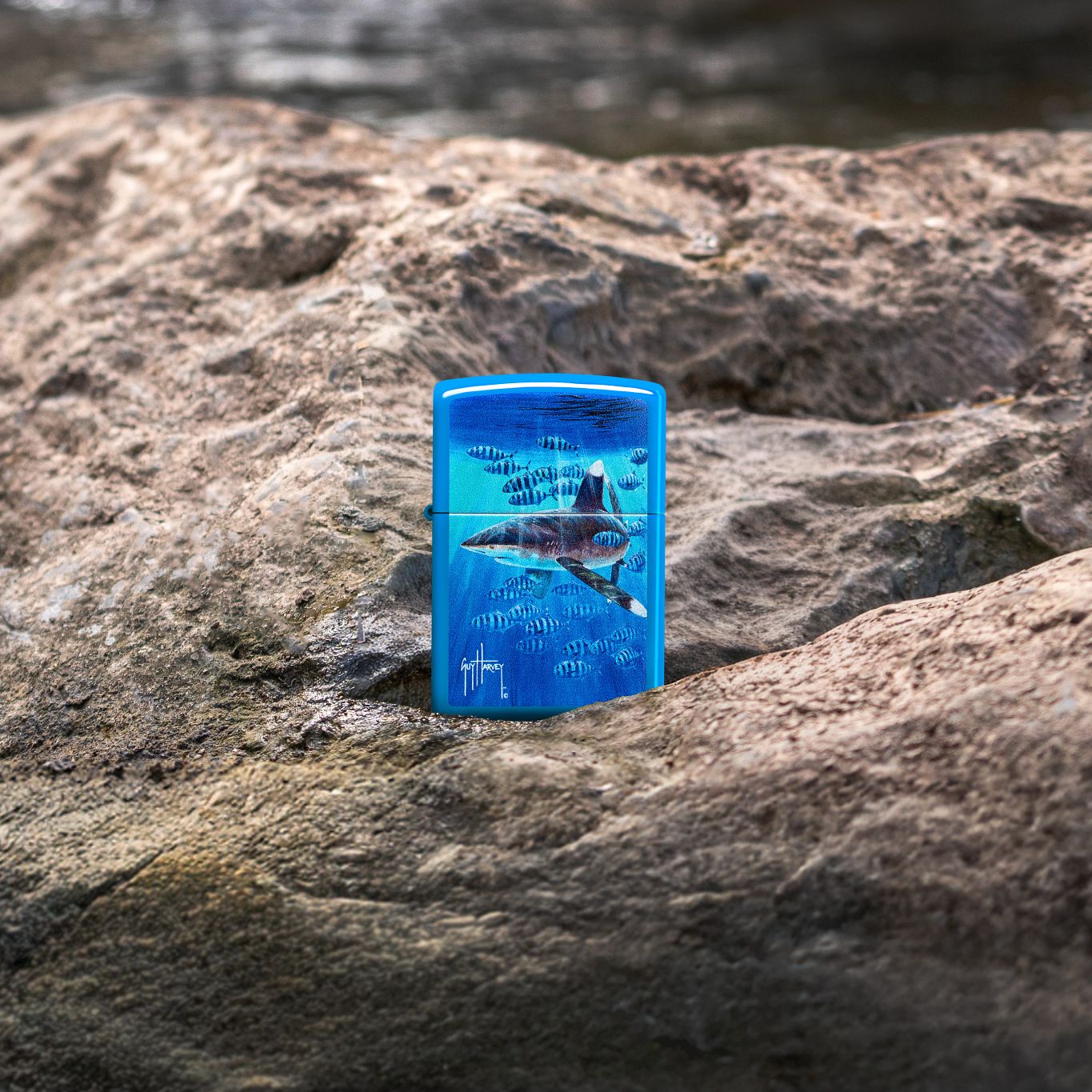 Lifestyle image of Zippo Guy Harvey Co-Pilot Design Sky Blue Matte Windproof Lighter standing on a rocky surface showing the front of the lighter. 

