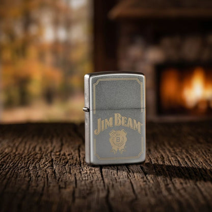 Lifestyle image of Zippo Jim Beam® Border Design Satin Chrome Windproof Lighter standing on a wooden table in front of an outdoor fireplace showing the front of the lighter. 

