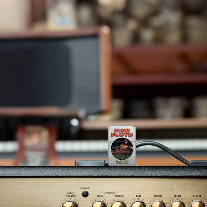 Lifestyle image of Zippo Pink Floyd Pyramids Design Street Chrome Windproof Lighter standing on a tube guitar amp with other equipment in the background, while showing the front of the lighter. 

