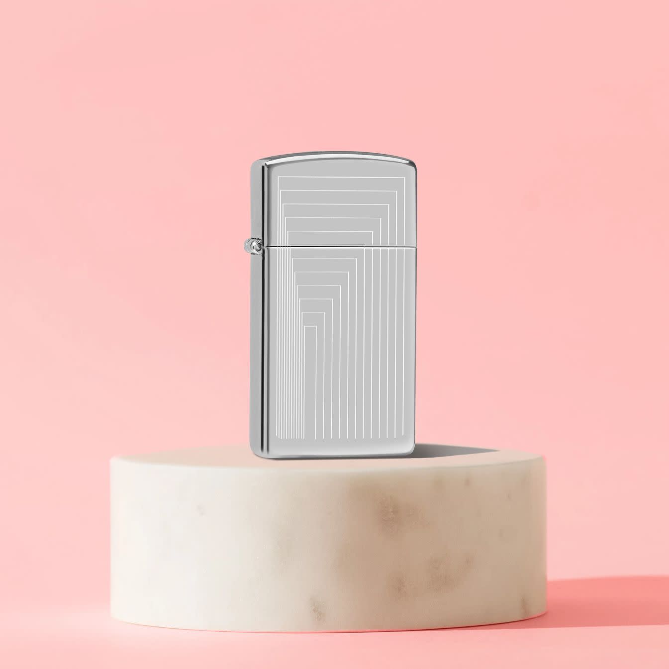 Lifestyle image of Zippo Slim® Laser Pattern Design High Polish Chrome Windproof Lighter standing on a cream-colored cylinder set against a light peach background.