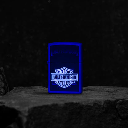 Lifestyle image of Zippo Harley Davidson® Black Light Purple Matte Windproof Lighter standing on a rock glowing under a black light.