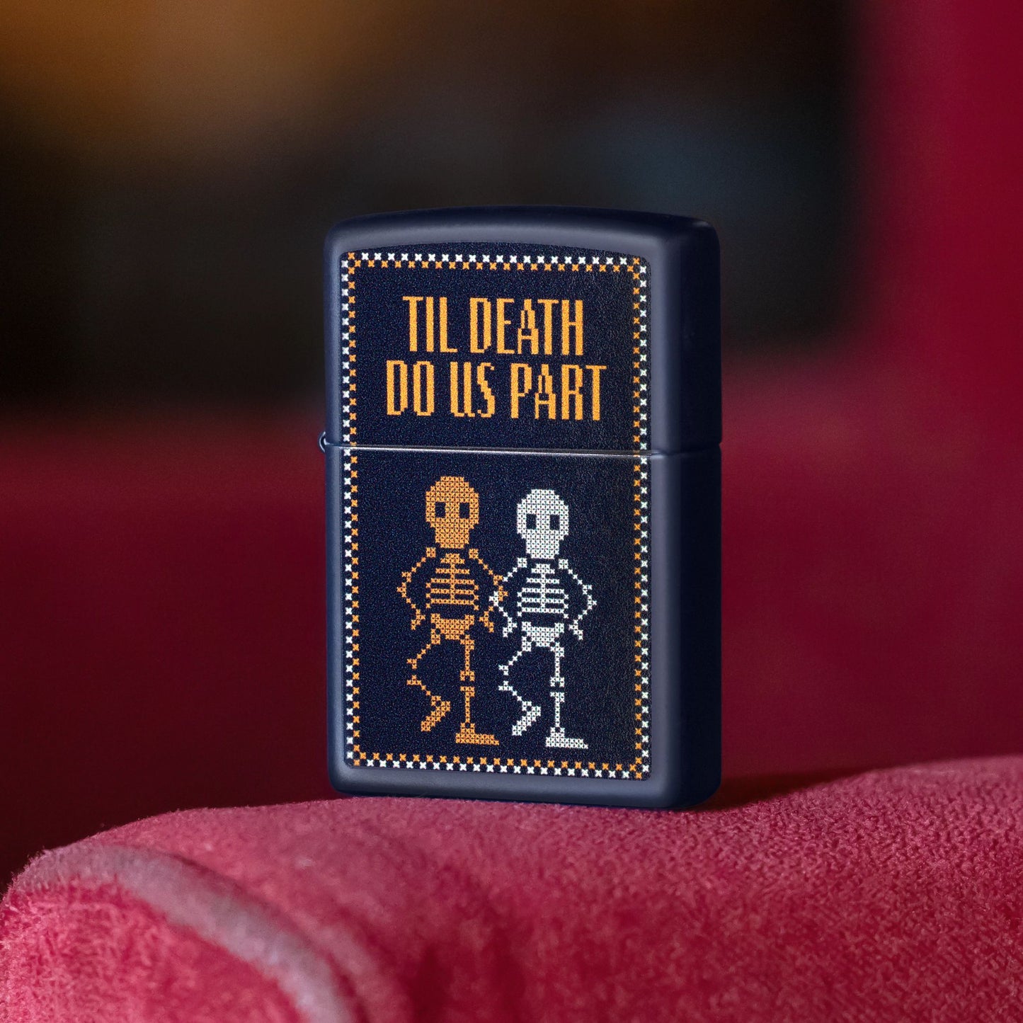 Lifestyle image of Zippo Til Death Do Us Part Design Navy Matte Windproof Lighter standing on the armrest of a red chair or sofa showing the front of the lighter. 

