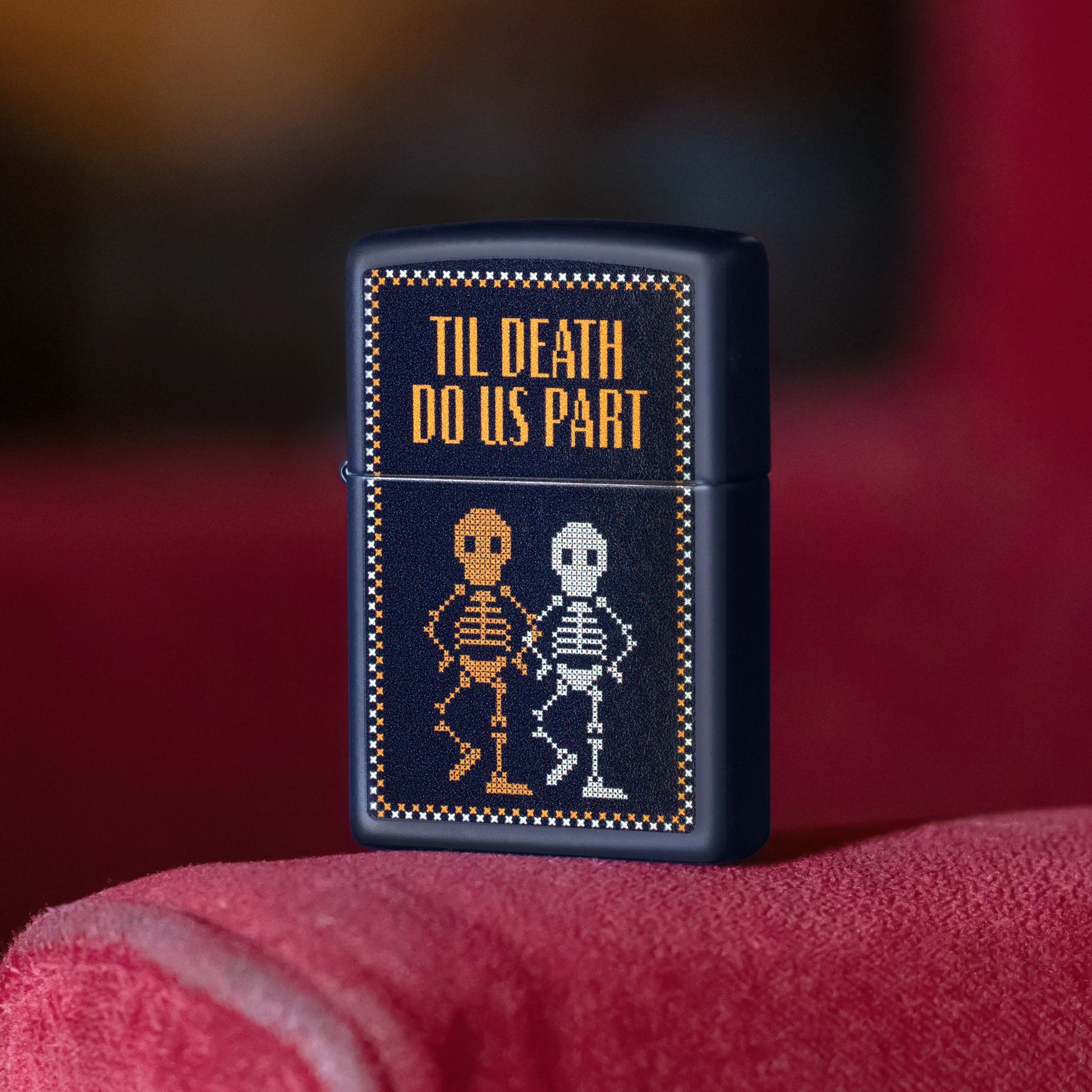 Lifestyle image of Zippo Til Death Do Us Part Design Navy Matte Windproof Lighter standing on the armrest of a red chair or sofa showing the front of the lighter. 

