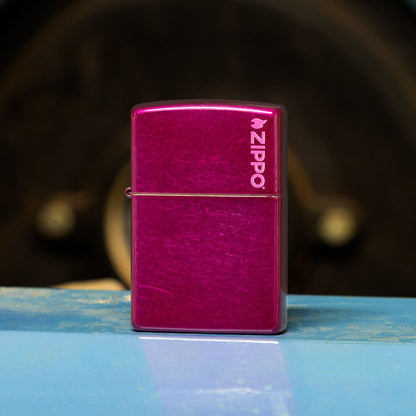 Lifestyle image of Zippo Classic Candy Raspberry Zippo Logo Windproof Lighter standing on a light blue metal bench showing the front of the lighter. 

