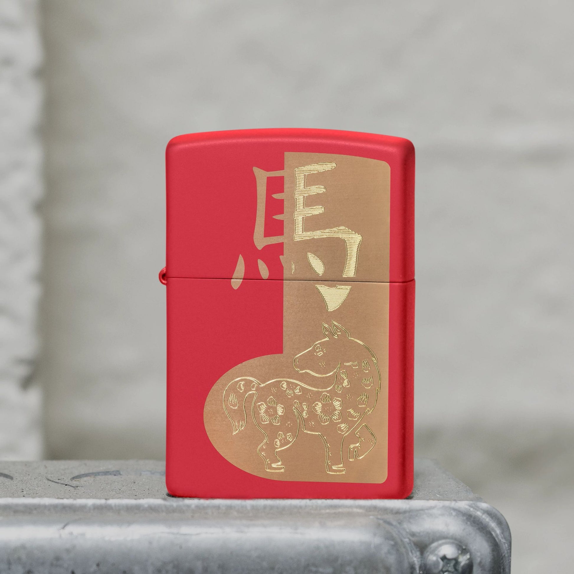 Lifestyle image of Zippo 2026 Year of the Horse Design Red Matte Windproof Lighter standing on a metal surface showing the front of the lighter. 

