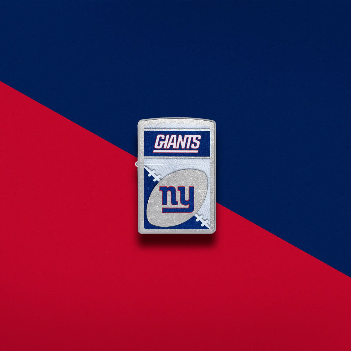 Lifestyle image of Zippo NFL New York Giants Street Chrome Windproof Lighter set on a navy and red background.