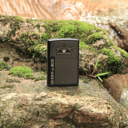 Lifestyle image of Zippo Queen Of Bud Line Design Black Matte Windproof Lighter standing on a group of mossy rocks.